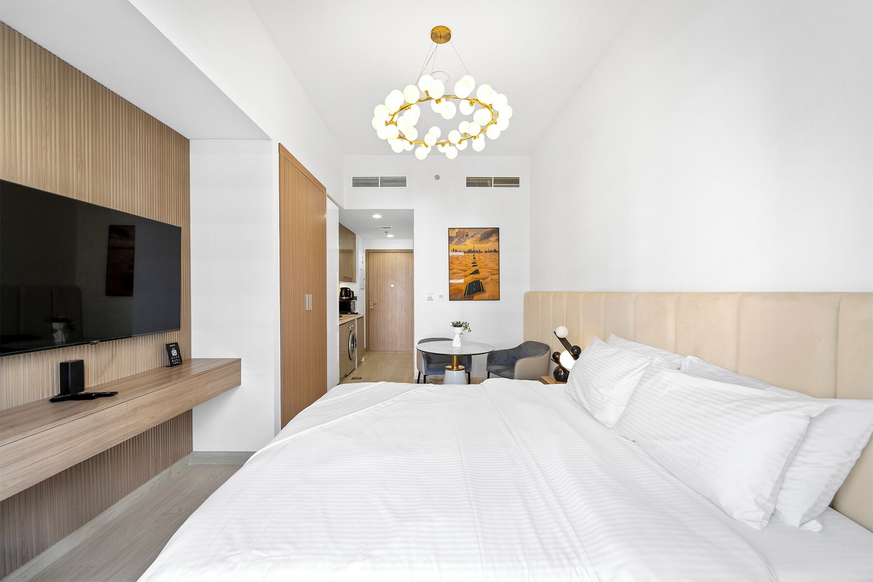 A modern hotel room with a large bed, a TV, a desk, and a dining area.