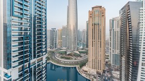 A high-rise building with a curved facade, surrounded by other tall buildings, a central roundabout, and a body of water. - Luxurious High-Floor 3BR with Assistant Room, Showcasing Lake & City Views (Dubai)