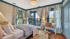 Ein Schlafzimmer mit einem Bett, zwei Vorhängen, einem Schreibtisch, einem Stuhl und einem gemusterten Teppich.