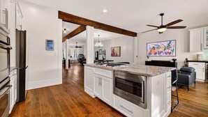 Una cucina moderna con mobili bianchi, un'isola centrale con forno integrato e una ventola a soffitto.