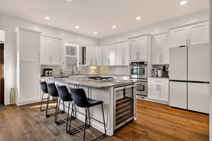 A modern kitchen with white cabinets, a central island with bar stools, and stainless steel appliances. - Savannah Getaway | Private Pool & Walkability to Everything by Lucky Savannah (Savannah)