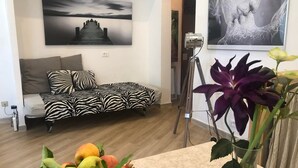 Ein Wohnzimmer mit einem zebra-gemusterten Sofa, einem Tisch mit Früchten und einer Blumenvase, sowie zwei Kunstwerken an den Wänden.