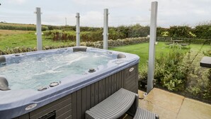 Un bain à remous avec un revêtement extérieur en bois, donnant sur une cour verdoyante et un mur de pierres.