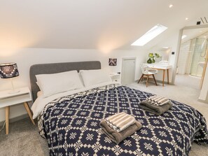 A bedroom with a large bed, a desk, and a shower area. - Cae Sam (Pentraeth)