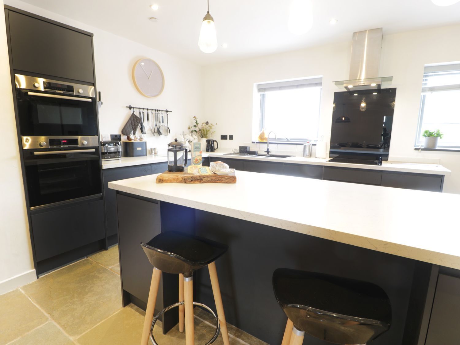 A modern kitchen with a central island, black cabinetry, stainless steel appliances, and a visible clock on the wall.