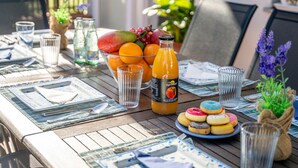 Una mesa de comedor preparada con platos, vasos, una botella de jugo de naranja y un bol de fruta.