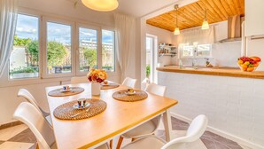 Un comedor con mesa de madera, sillas blancas y un jarrón de flores.