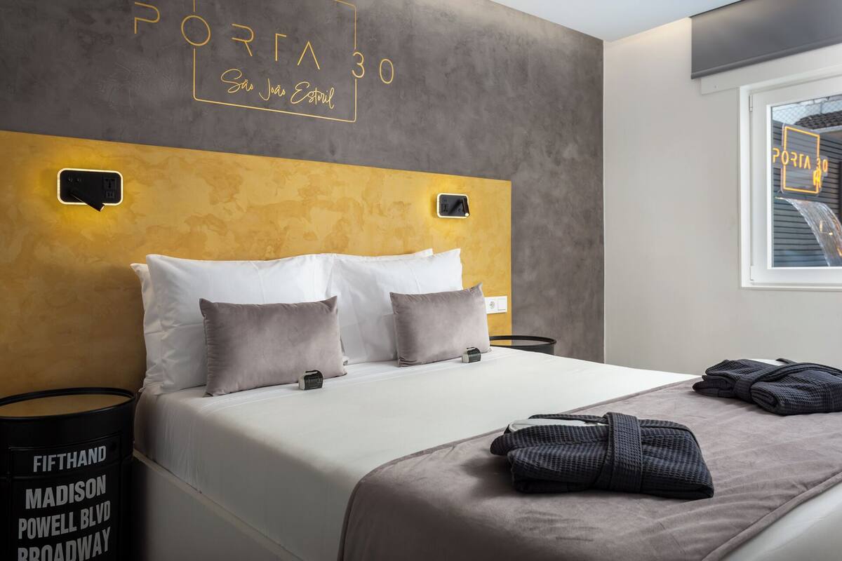 A hotel room with a large bed, two bedside tables, a wall-mounted light, and a window with a view of the outside.