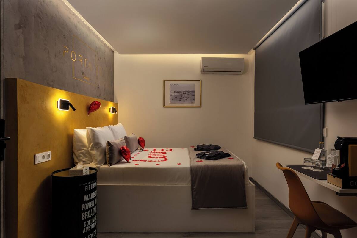 A hotel room with a bed, bedside table, chair, and a TV on the wall.
