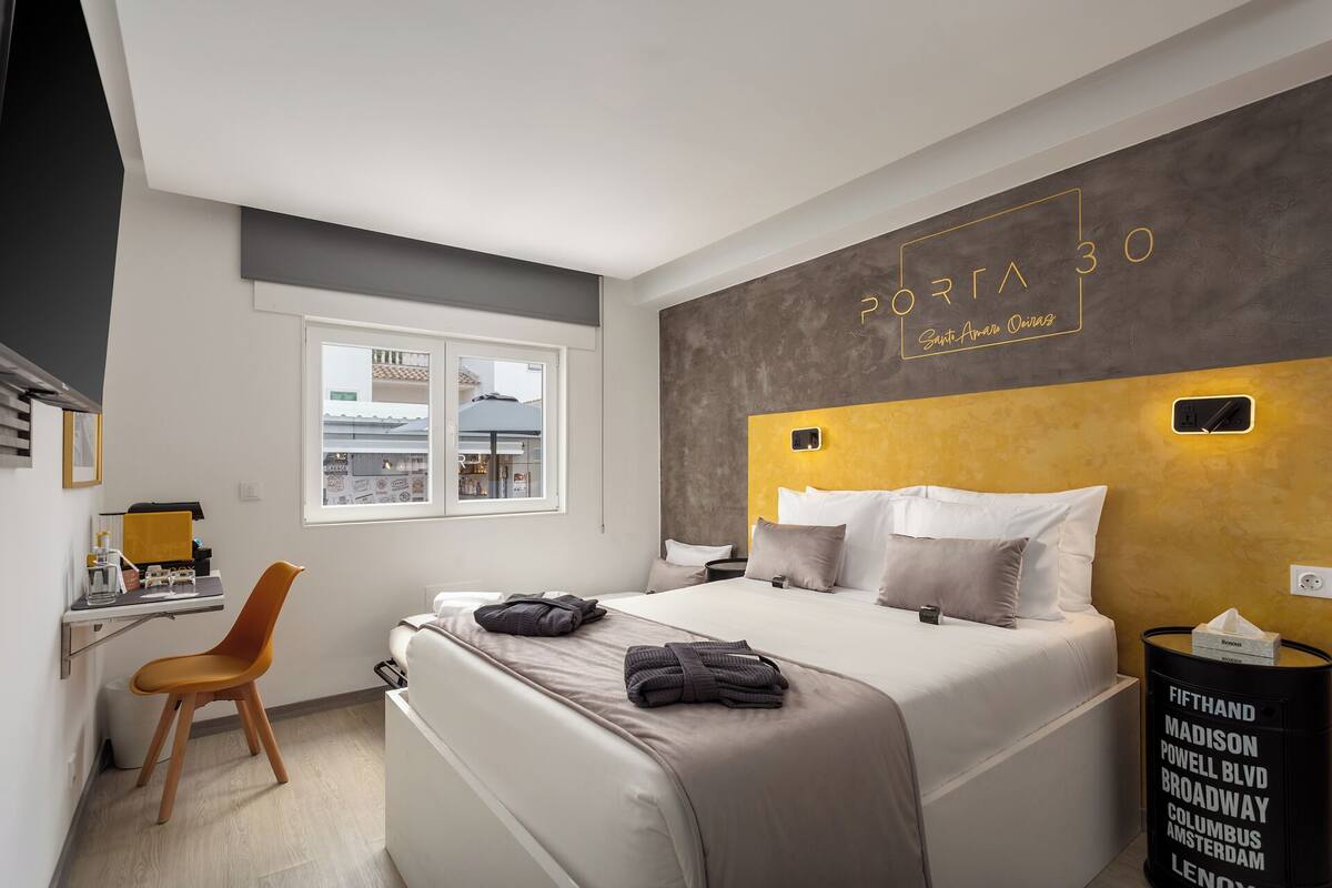 A modern hotel room with a bed, a desk, and a chair. There is a window with a view of the street.