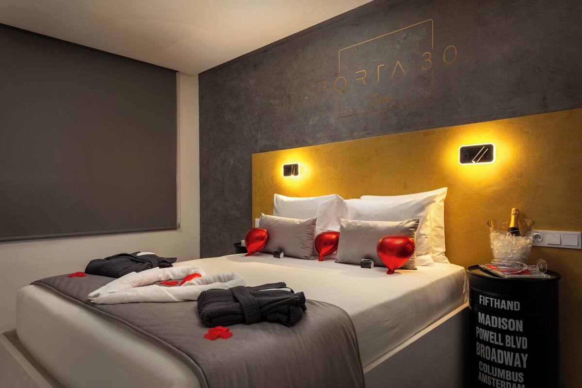 A modern hotel room with a large bed, a minibar, and a wall-mounted light fixture.