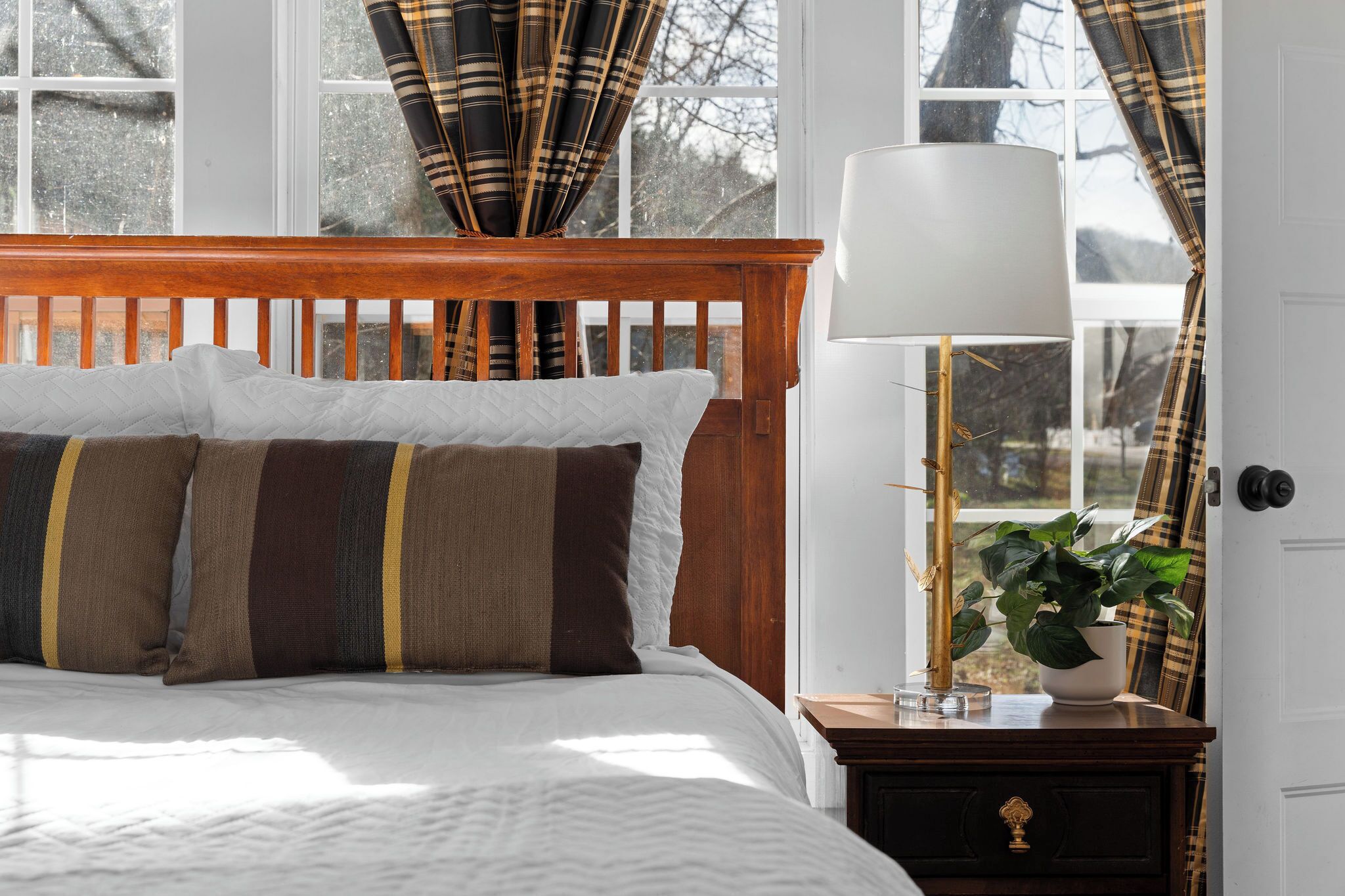 Une chambre à coucher avec une tête de lit en bois, un lit avec des oreillers à rayures, une table de chevet avec une lampe et une plante en pot.