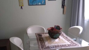 A dining area with a glass table, white chairs, and a decorative bowl. - Apto Pet Friendly com Garagem na Praia do Morro (Guarapari)