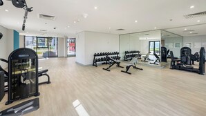 A modern gym with various exercise equipment, large windows, and a clean, spacious layout. - Stylish Studio with Garden Views (Dubai)