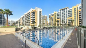 A swimming pool with lounge chairs and a lifeguard stand, surrounded by modern apartment buildings. - Stylish Studio with Garden Views (Dubai)