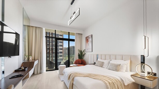 A modern hotel room with a large bed, a desk, a television, and a view of the city through large windows. - Stylish Studio with Garden Views (Dubai)