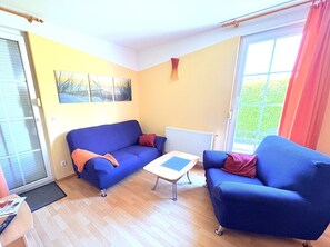 Ein Zimmer mit einem blauen Sofa, einem kleinen Tisch, einer Heizung und einem Fenster mit Blick ins Grüne.