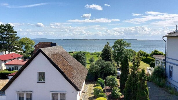 Ett vitt hus med ett halmtak, utsikt över en sjö och en klar himmel.