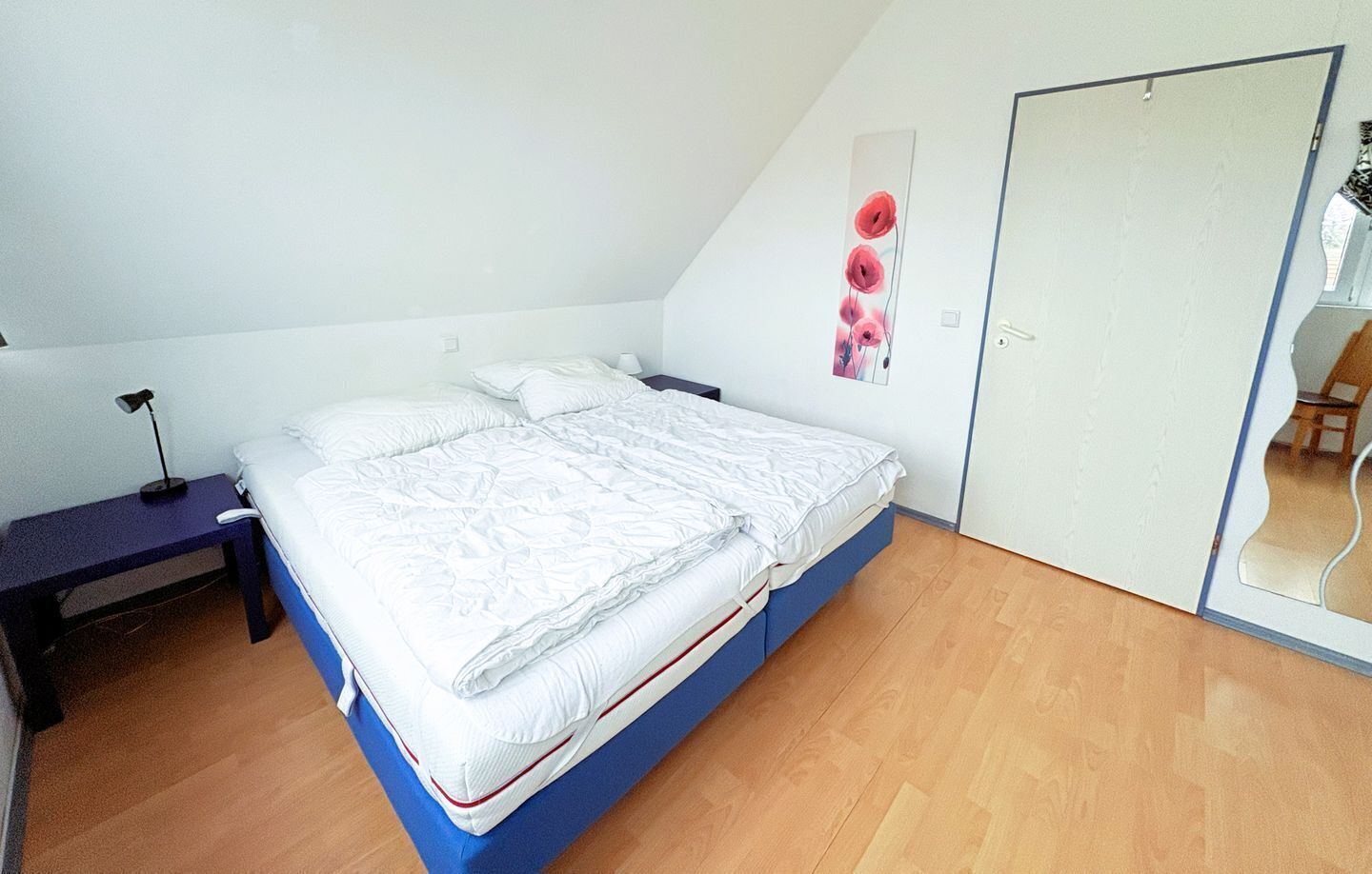A bedroom with a single bed, a nightstand, a desk, and a mirror.