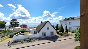 Ett bostadsområde med ett vitt hus som har ett brant tak, en asfalterad uppfart och utsikt över en vattenyta i bakgrunden.