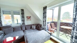 Ett modernt loftrum med ett stort fönster, en bäddsoffa och en balkong med utemöbler.