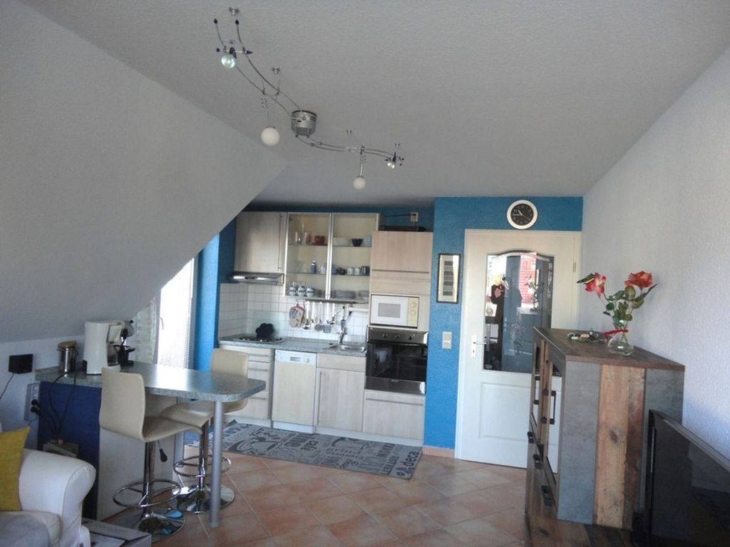 A compact kitchen with modern appliances, a dining area with bar stools, and a living space with a sofa and a TV.