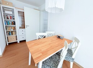 Huoneessa on puinen ruokapöytä, valkoiset tuolit, kirjahylly ja valkoinen ovi.