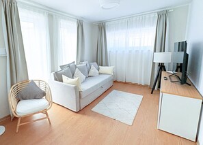 Moderni olohuone, jossa on sohva, nojatuoli, lamppuvarustettu työpöytä ja televisio.
