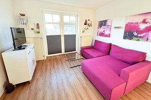 A room with a pink sofa, a white cabinet with a television, and a sliding glass door leading to an outdoor area. - Apartment 15 in Haus Hühnergott - pet-friendly and modern - Holiday apartment 15 - (Sellin)