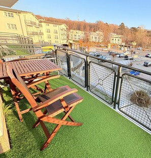 A balcony with a wooden table and chairs, surrounded by a metal fence, overlooking a parking area and buildings. - Apartment 15 in Haus Hühnergott - pet-friendly and modern - Holiday apartment 15 - (Sellin)