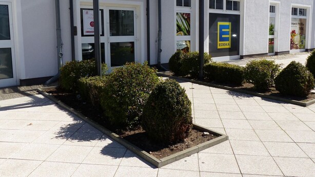 En byggnad med en vit fasad, en blå skylt med texten ”EDEKA” och en överbyggd entré.