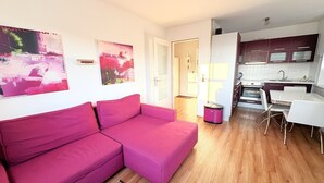 En modern lägenhet med en rosa soffa, ett kök med mörka skåp och en matplats med vita stolar.