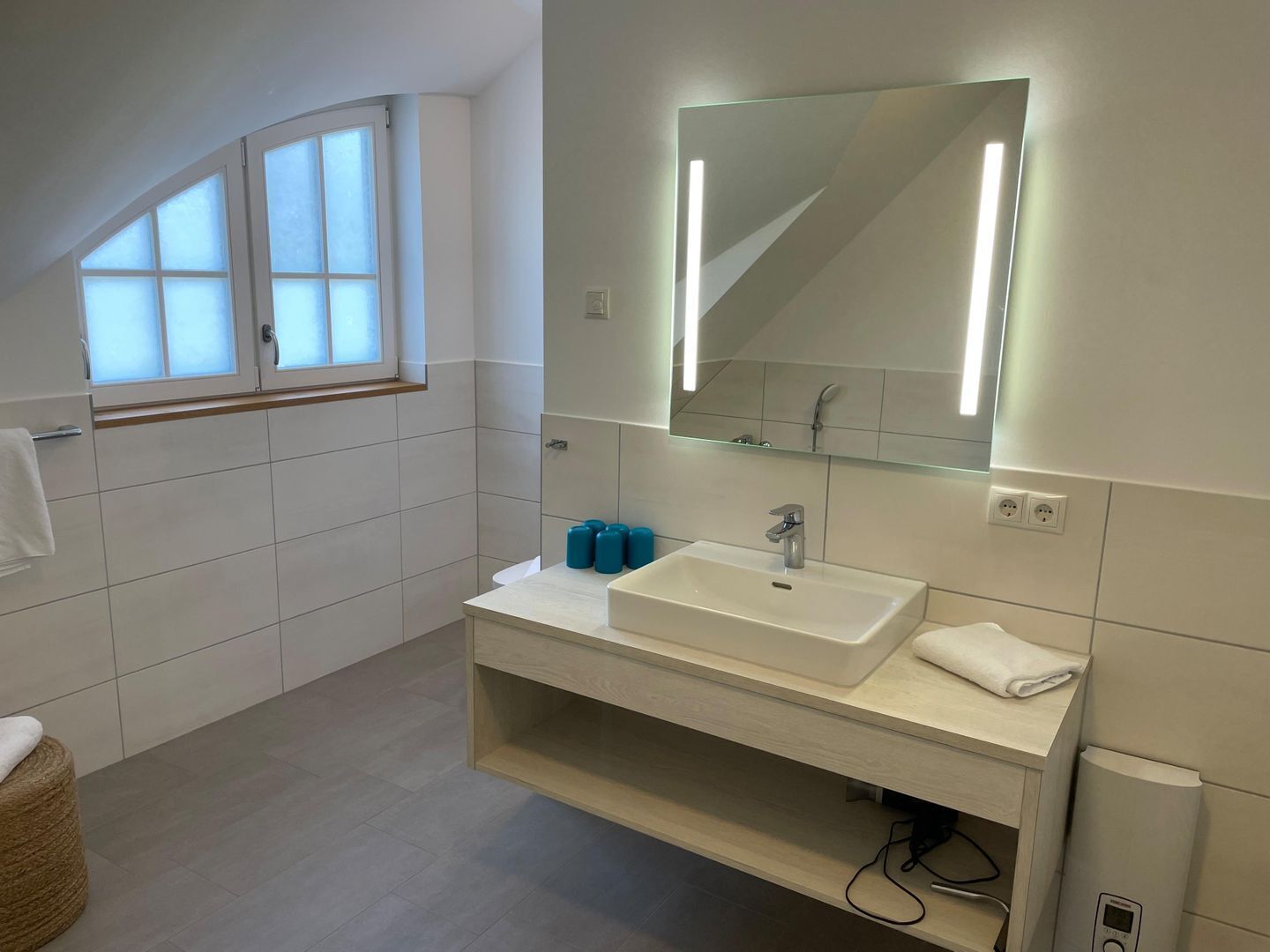 A modern bathroom with a large window, a white sink, a mirror, and a towel rack.