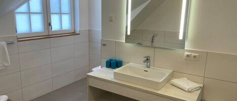 A modern bathroom with a large window, a white sink, a mirror, and a towel rack.
