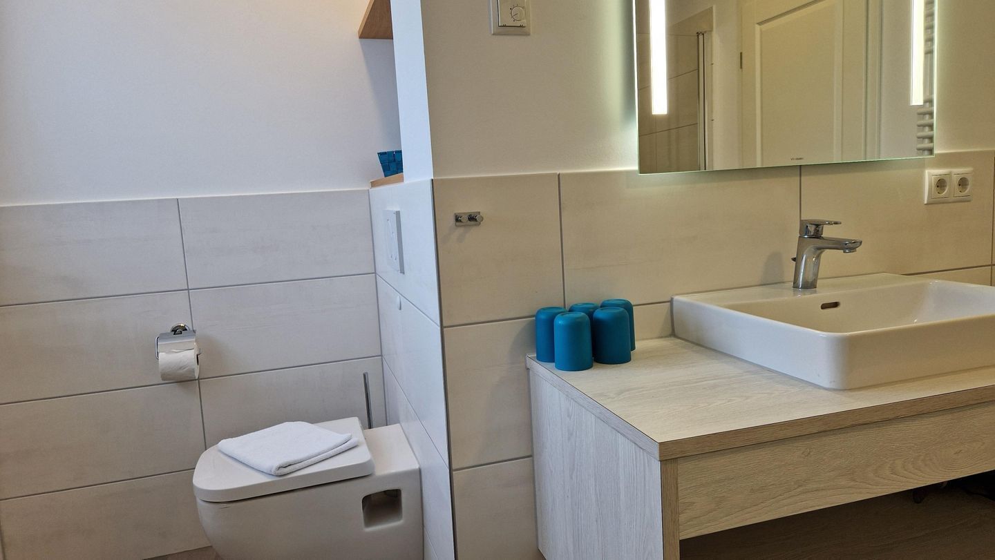 A bathroom with a toilet, sink, mirror, and blue soap dispensers.