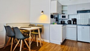 Eine kleine Küche mit weißen Schränken, einer Mikrowelle, einer Kaffeemaschine und einem Essbereich mit Tisch und Stühlen.