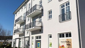 Ein mehrstöckiges Gebäude mit Balkonen, einem Schild, das auf den Verkauf von frischen und verarbeiteten Lebensmitteln hinweist, und einem strahlend blauen Himmel.