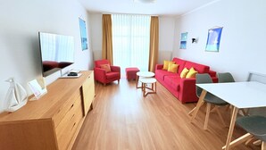 Ein modernes Wohnzimmer mit einem roten Sofa, einem Holztisch, einem Fernseher und einem Essbereich mit einem weißen Tisch und Stühlen.