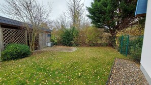 Ein Garten mit Rasen, einem Holzschuppen, einem grünen Zaun und einem Baum.