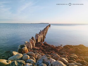 Un paisaje costero con un largo muelle de piedra que se adentra en aguas tranquilas, rodeado de una costa rocosa.