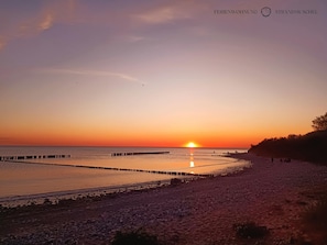 Une plage au coucher du soleil, avec une jetée qui s’avance dans l’eau.