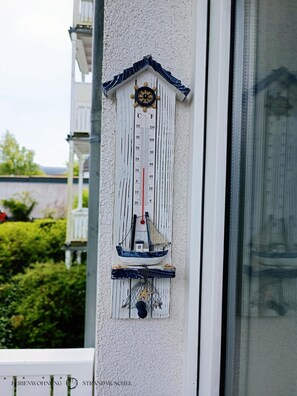 Un thermomètre décoré d’un motif représentant un navire et des étoiles de mer, fixé au mur.