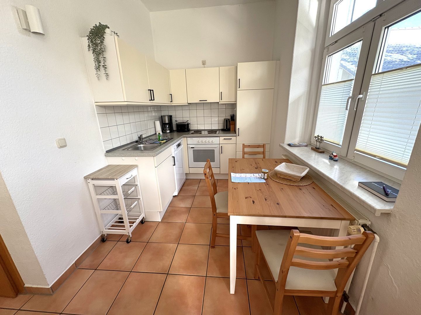 A compact kitchen with white cabinets, a wooden table, and a window with blinds.