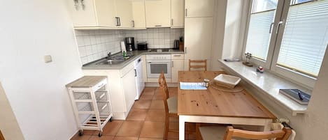 A compact kitchen with white cabinets, a wooden table, and a window with blinds.