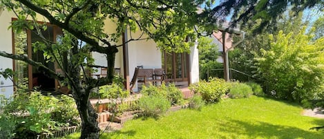 A garden with a wooden deck, a lawn, and a building with large windows.