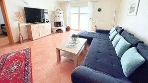 Ein Wohnzimmer mit einer Couch, einem Fernseher, einem Kamin und einem großen Fenster.