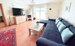 A living room with a sofa, a TV, a fireplace, and a large window. - Ginster vacation apartment - with conservatory and large property - Holiday apartment (Mariendorf)