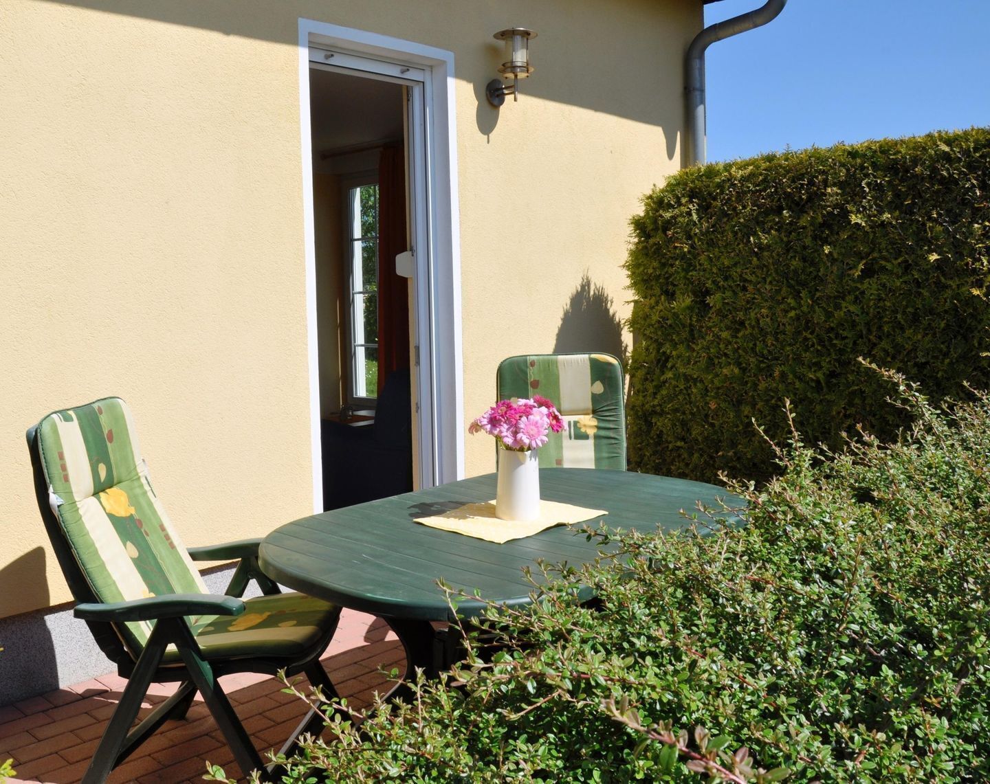 An outdoor patio with a round table, two chairs, and a vase with flowers.
