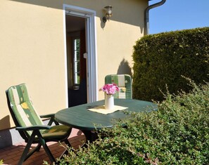 Eine Terrasse im Freien mit einem runden Tisch, zwei Stühlen und einer Vase mit Blumen.
