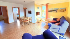 A living room with a sofa, a dining table with chairs, a TV, and a window with curtains. - Fewo Seelenfrieden 2 - with terrace and parking space - Sunny vacation apartment for (Alt Reddevitz)